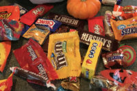 Close-up of a heaped pile of assorted wrapped Halloween candy bars with a small orange pumpkin among them.