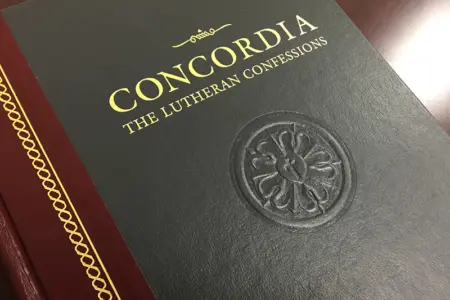 Concordia: The Lutheran Confessions, the black and gold hardcover from Concordia Publishing House, embossed with a Luther rose and resting on a wooden table