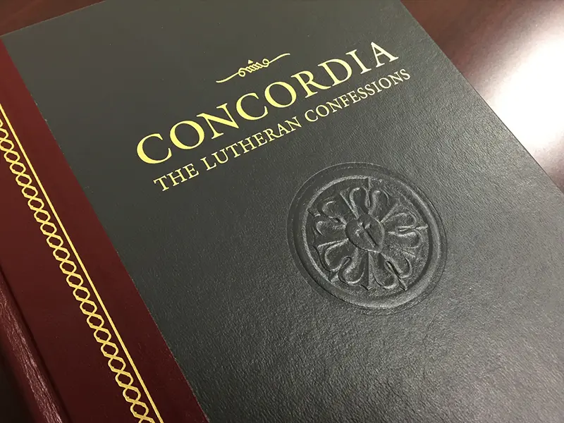 A copy of Concordia: The Lutheran Confessions resting on a wooden table, its black and gold cover embossed with the Luther rose.